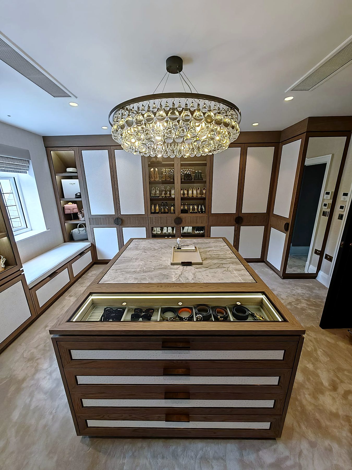Fitted dressing room with oak wardrobes, stone-topped island and chandelier