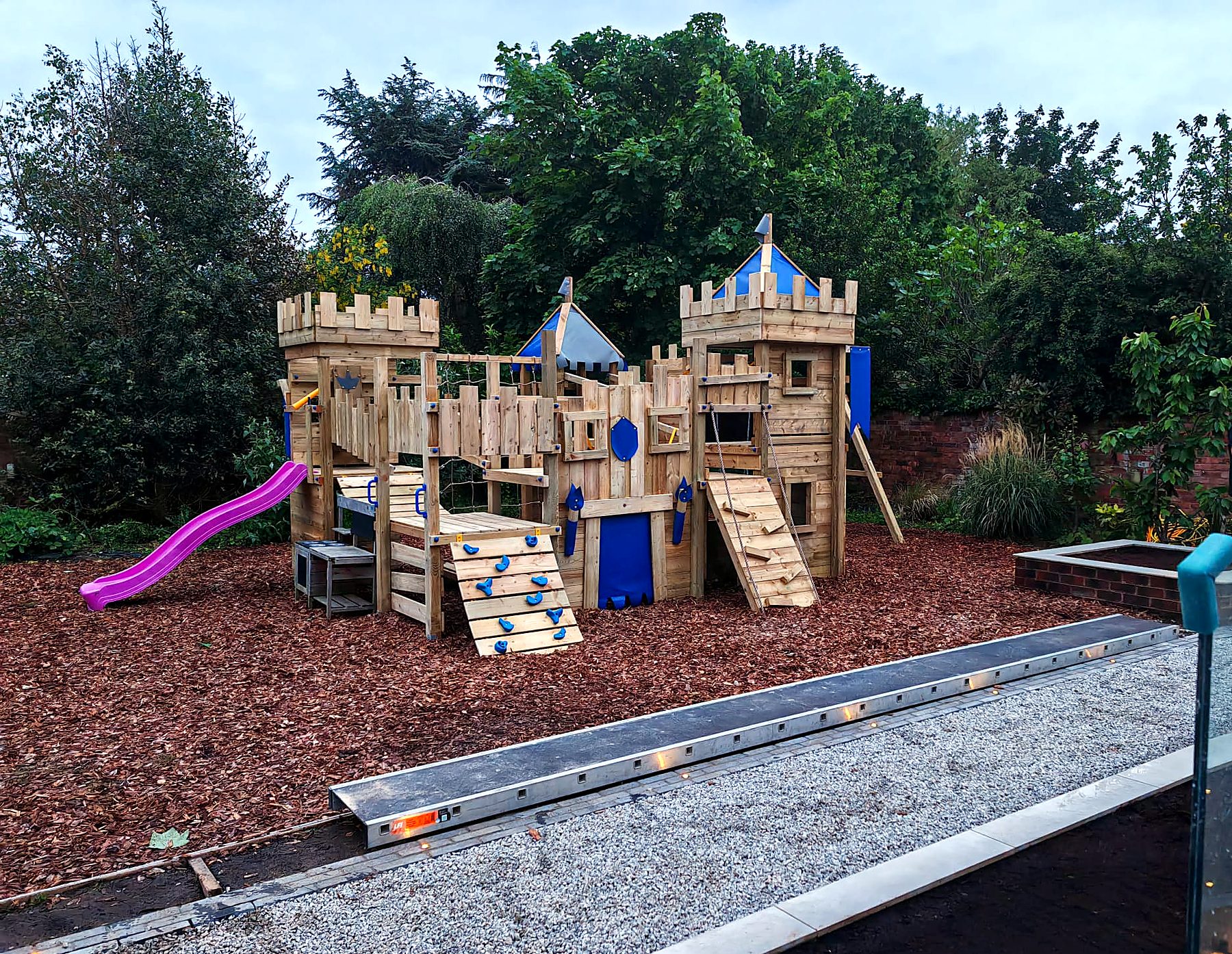 Landscaped garden with timber play castle, bark surface and lit stone edging