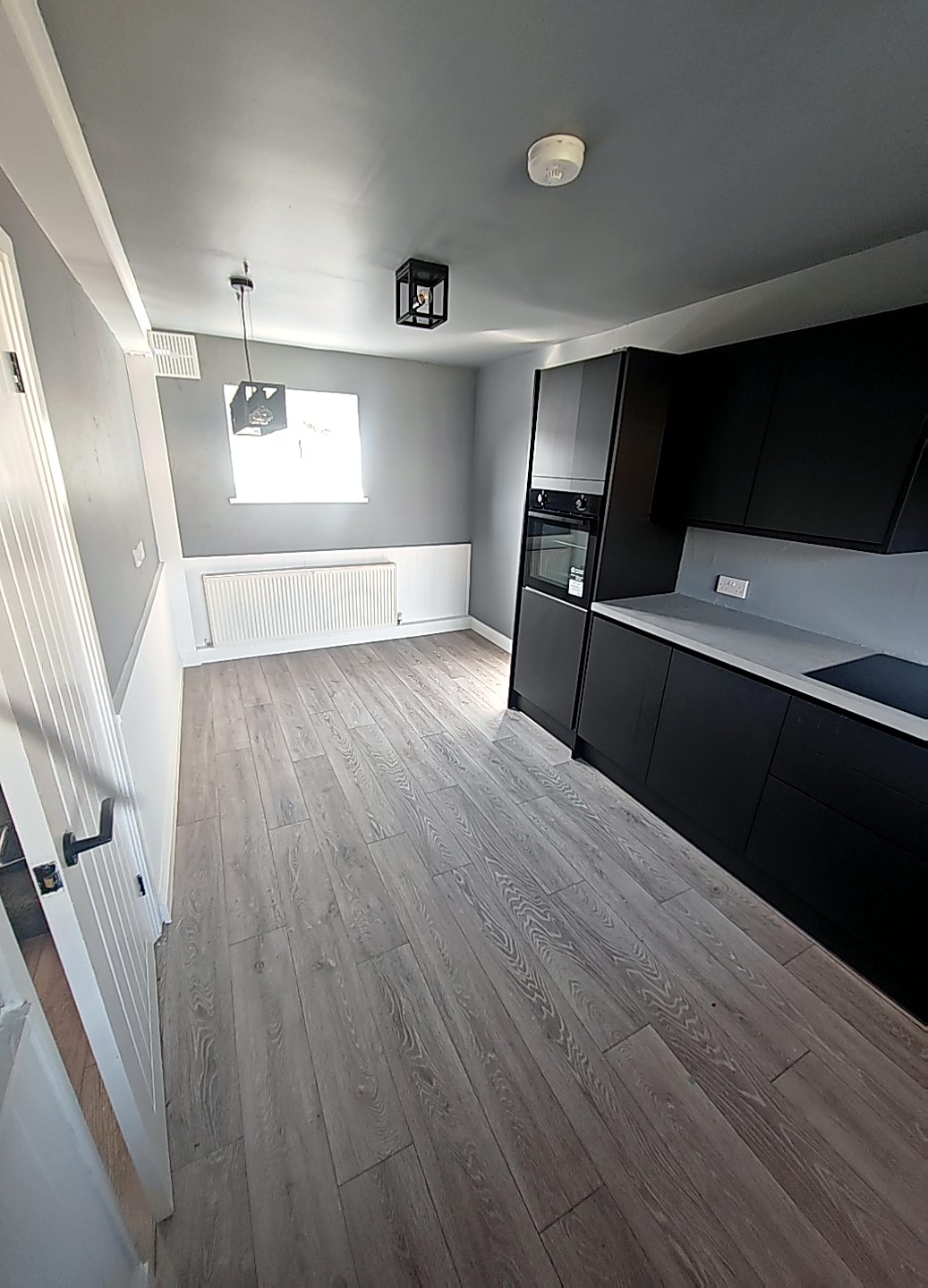 Refurbished kitchen diner with matt black units and grey wood-effect flooring